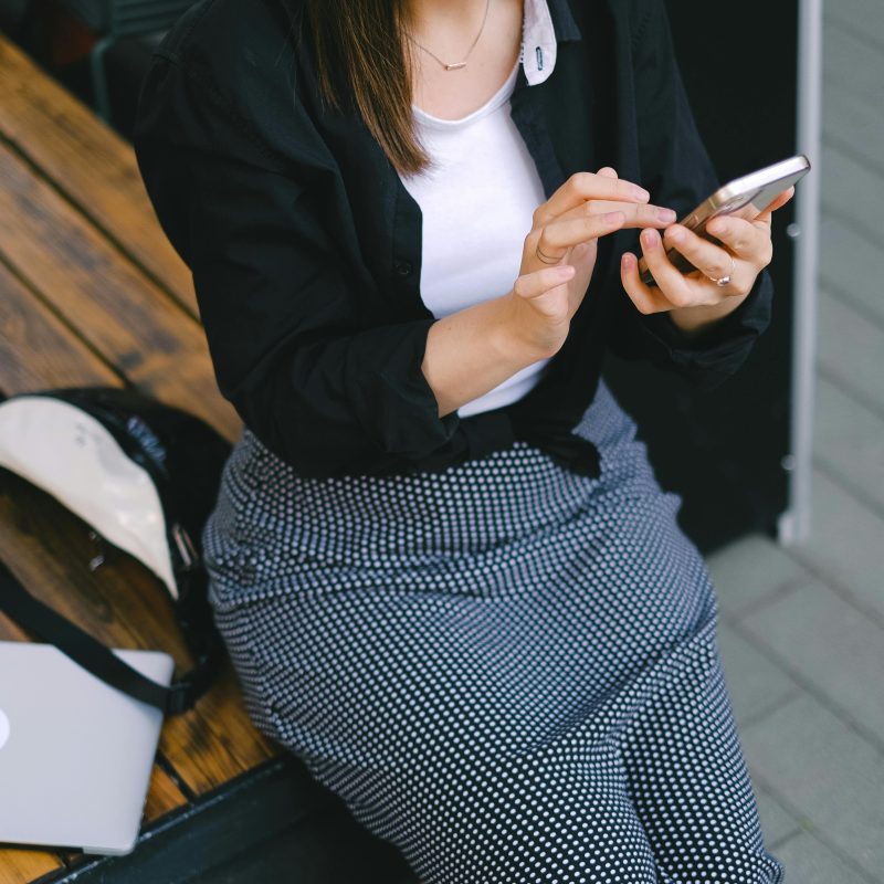 A stylish woman sits outdoors using her smartphone, embodying modern freelance lifestyle.